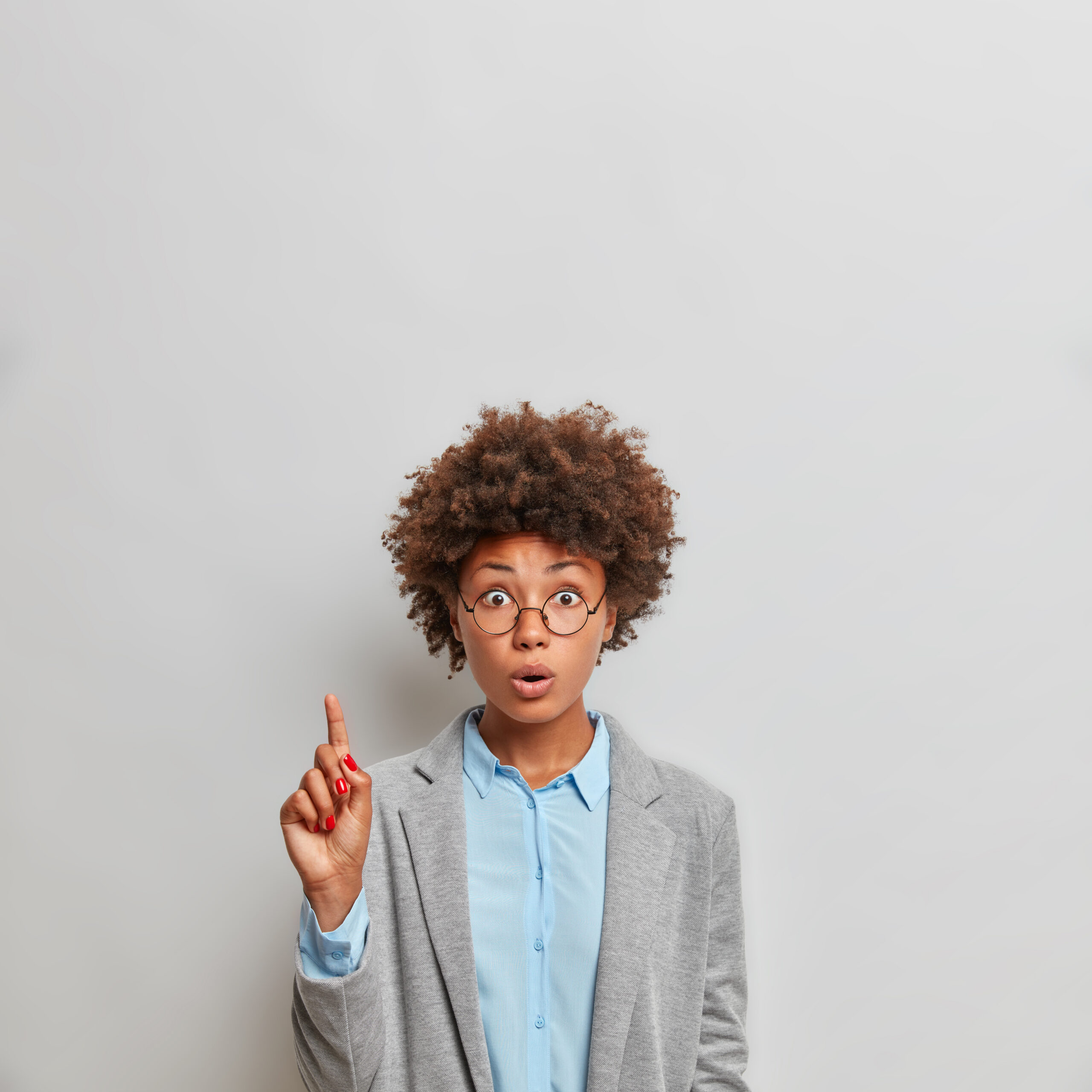 vertical shot of surprised young afro american business lady dressed in formal elegant clothes points above on copy space isolated over grey background astonished by something. look upwards.